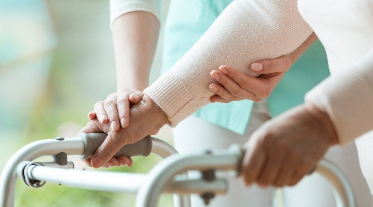 Osoba pomagająca chodzić drugiej osobie z balkonikiem